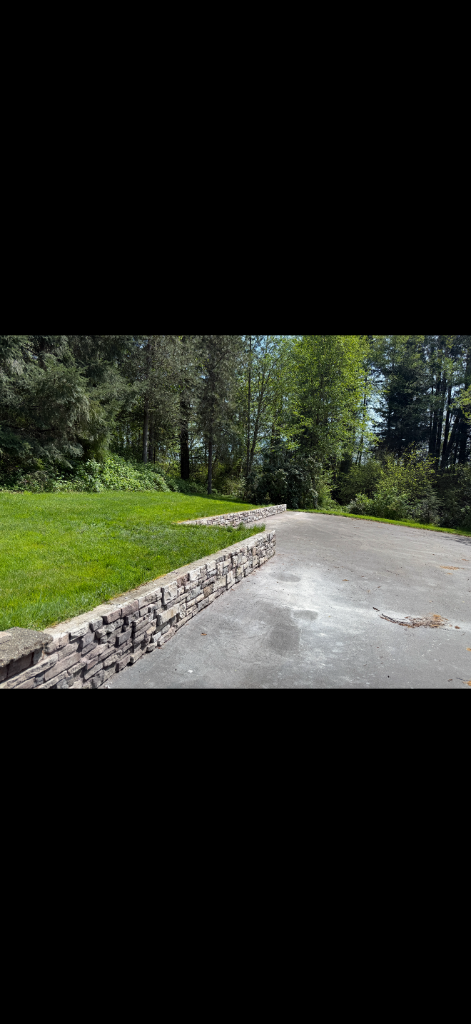 Stone retaining wall along curved driveway by DNT Masonry